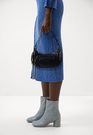 Bolso de cuero negro con acentos dorados y una correa de cadena, que cuenta con un bolsillo con cremallera en la parte frontal. Combinado con un vestido azul de canalé y botas de tobillo grises.