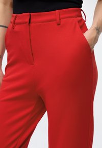 Rote, maßgeschneiderte Hose mit glatter Textur, ausgestattet mit Seitentaschen und Gürtelschlaufen. Abgebildet von der Taille abwärts, um die Passform hervorzuheben.