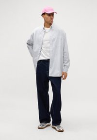 Camisa a rayas de botones en blanco y azul con un corte relajado, combinada con unos vaqueros de pierna ancha de color azul oscuro y zapatillas plateadas; lleva una gorra rosa.