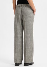 Graue karierte weite Hosen aus strukturiertem Stoff mit elastischem Bund, Seitentaschen und schwarzen kontrastierenden Absatzschuhen.