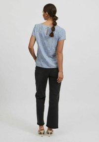 Top de color azul claro, de manga corta, con un patrón texturizado y detalle en la espalda en forma de llave; combinado con unos jeans negros y zapatos de tacón beige.