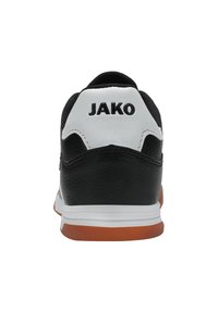 Scarpa sportiva bianca e nera con tomaia in pelle strutturata, suola arancione e il marchio "JAKO" ben visibile sul tallone. Design semplice.