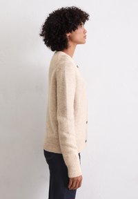 Beige gebreide cardigan met lange mouwen, geribbelde manchetten en een knoopsluiting aan de voorkant. Zachte textuur, relaxte pasvorm en subtiele kleurvariatie.