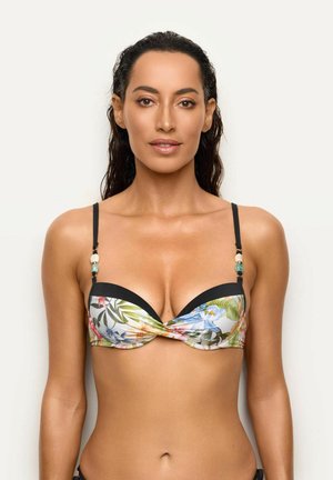 Kobieta o długich ciemnych włosach nosząca kolorowy kwiatowy top od bikini z czarnymi ramiączkami i detalami z koralików na gładkim jasnym tle.