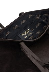 Schwarze Wildleder-Shopper-Tasche mit Lederakzenten, ausgestattet mit einer Reißverschlusstasche und einem gebrandeten Innenfutter. Strukturierte Griffe und polierte Beschläge.