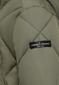 Olijfgroene, gestikte jas met een gladde textuur, opvallende stiksels en een label met de tekst "FRIEDA FREDDIES NEW YORK."