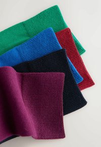 Gestapelte gestrickte Ärmel in Grün, Blau, Rot, Schwarz und Lila, diagonal auf einer hellen Oberfläche ausgelegt.