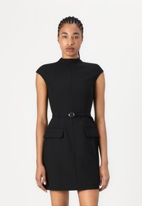Robe noire ajustée avec un col montant et des manches courtes, présentant une taille ceinturée et deux poches avant. Tissu lisse et design structuré.