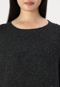 Pull en laine gris foncé avec une finition texturée, doté d'un col rond côtelé et de manches longues. Vue en gros plan de la texture du tissu.