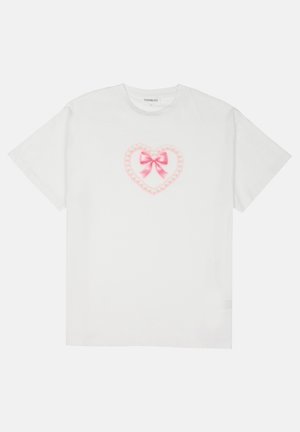 Weißes Baumwoll-T-shirt mit einem pinken Herzdesign, das mit einer Schleife und Kettendetails versehen ist. Kurze Ärmel und ein runder Ausschnitt. Weiche Textur.