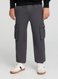 Szare spodnie cargo z dwoma bocznymi kieszeniami, luźnym krojem i widocznymi detalami przeszyć. W zestawieniu z białymi trampkami z czarnymi akcentami.
