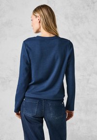 Marineblaues Langarmoberteil mit einem strukturierten Karomuster, kombiniert mit dunkelblauen Jeans mit Gesäßtaschen und Nähten.