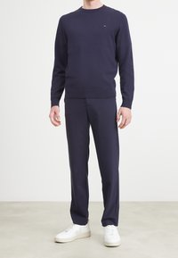 Granatowy sweter z okrągłym dekoltem i ściągaczem na dole, w zestawie z dopasowanymi granatowymi spodniami i białymi sneakersami; gładka tekstura, minimalne logo na swetrze.