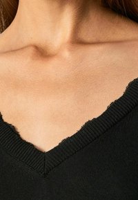 Maglietta nera a maglia con scollatura a V, caratterizzata da un bordo a ondulazione sul collo. Tessuto liscio con una silhouette aderente e senza decorazioni.