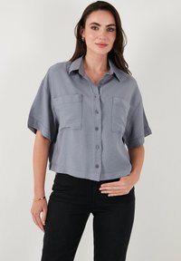 Cropped gray blouse with a button-up front, collar, and two chest pockets. Fabric is lightweight with a smooth texture.