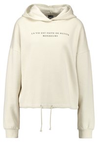 Krämfärgad hoodie med dragsko i nederkant, oversized passform och tryckt fransk text på framsidan. Mjuk material och ribbade ärmslut.