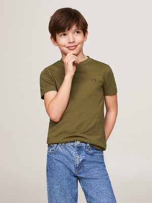 T-shirt à manches courtes vert olive avec un petit logo sur la poitrine, associé à un jean en denim bleu clair avec une coupe classique et un léger effet d'éraflure.