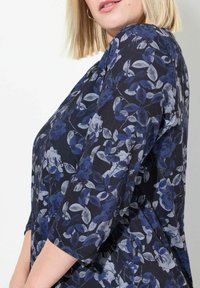 Bloes met bloemenpatroon en driekwart mouwen, met een marineblauwe achtergrond, blauwe en grijze rozen, en zachte, lichte stof.