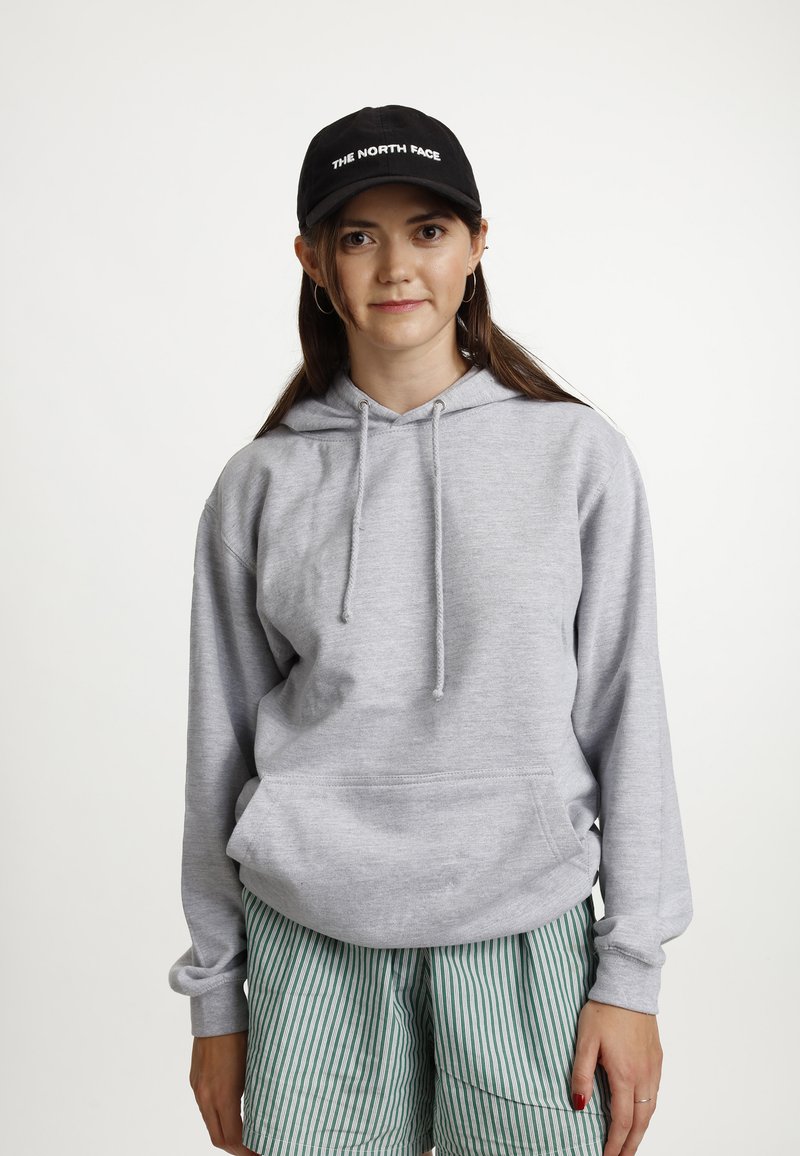 Grijze hoodie gemaakt van zachte stof, met een kangoeroezak en trekkoorden. Gecombineerd met groene gestreepte shorts en een zwarte pet.