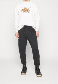 Vit sweatshirt med svart "Air Jordan" grafisk tryck, matchad med svarta jogger-byxor, med elastisk midja och sidofickor. Svarta sneakers.