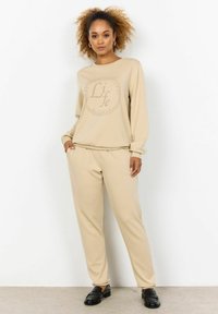 Beige Sweatshirt und passende Jogginghosen aus weichem Material, mit einem kreisförmigen Grafikdesign und dem Wort "Life". Lockere Passform, elastische Bündchen und Bund.