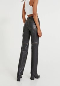 Pantalons en cuir noir avec une texture lisse, design à jambes droites, taille haute et détails de couture visibles. L'arrière comporte deux poches.