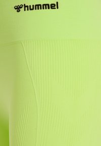 Ljust gröna atletiska leggings med ett texturerat mönster, som har en slät yta och en svart logotyp vid midjan.