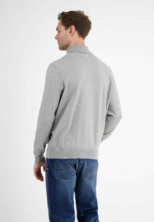 Grå strikket sweater med høj krave, ribbede manchetter og kant, båret med blå denimjeans. Stoffet er glat og tætsiddende.