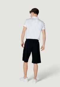 Polo bianco a maniche corte abbinato a pantaloni neri fino al ginocchio. Sneakers bianche. Vista posteriore, che mostra la cintura elastica e il dettaglio laterale.