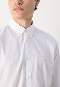 Weißes Hemd aus Baumwolle mit strukturierter Oberfläche, ausgestattet mit einem klassischen Kragen und einem auf der Brust gestickten Logo.