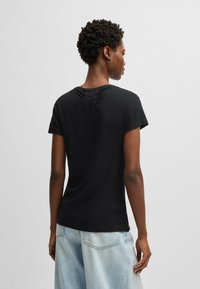 T-shirt nera a maniche corte con scollo rotondo e delicati dettagli di plissettatura sul retro, abbinata a pantaloni a gamba larga in denim chiaro.