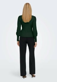 Green ribbed knit pullover with puff sleeves, paired with black straight-leg trousers and strappy black heels, model facing away.
