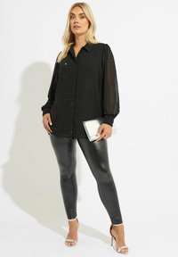 Blusa nera trasparente con maniche lunghe a palloncino, motivo a pois argentati, abbinata a leggings neri in ecopelle e sandali con tacco alto argentati.