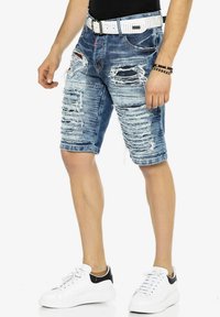 Helle blaue Jeansshorts mit ausgefransten Kanten und dezent ausgefransten Stellen. Kombiniert mit einem weißen Gürtel und Sneakers mit schwarzen Akzenten.