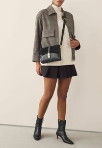 Giacca a quadri grigia, dolcevita crema in maglia, gonna nera a pieghe e stivaletti neri alla caviglia. Borsa a tracolla nera abbinata con dettagli dorati.