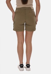 Pantaloni cargo verde oliva con tasche laterali, design aderente, orlo arrotolato e tessuto morbido e leggero. Sneakers bianche con dettagli neri.