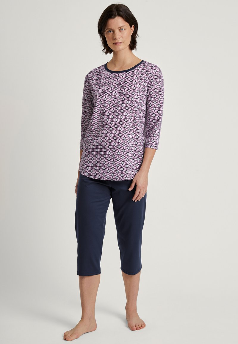 Paarse gebloemde top met een ronde halslijn en driekwartmouwen, gecombineerd met marineblauwe cropped broek. Zacht materiaal, losse pasvorm.