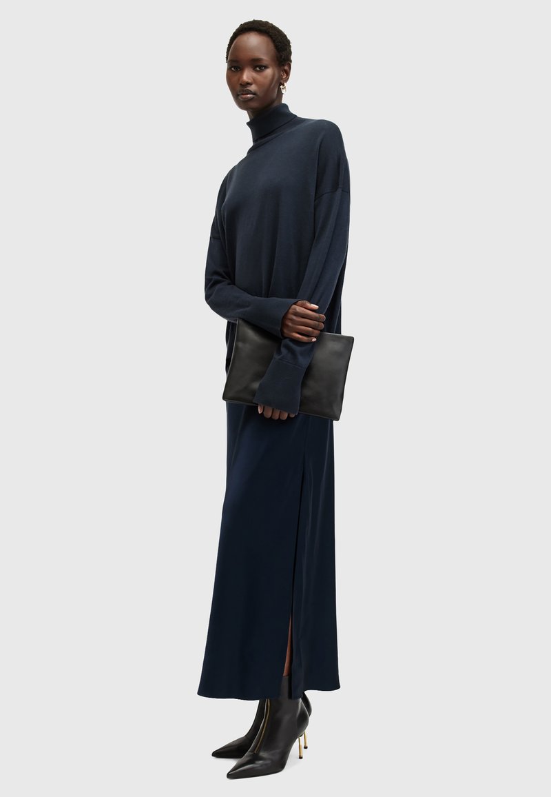 Marineblå turtleneck genser sammen med et langt marineblå skjørt med en sidelåst. Modellen holder en svart clutch og har på seg svarte hælankleboots.