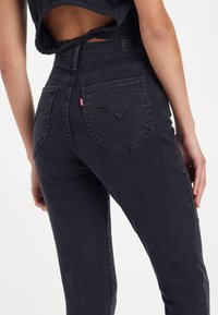 Høyt liv svart denimjeans med smal passform, med et særpreget hjerteformet baklomme-design og subtil falming.