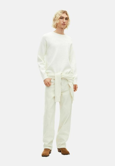 Hvid langærmet sweater parret med løse hvide bukser, der er bundet i taljen. Blød tekstur med et simpelt design. Brune sko fuldender outfittet.