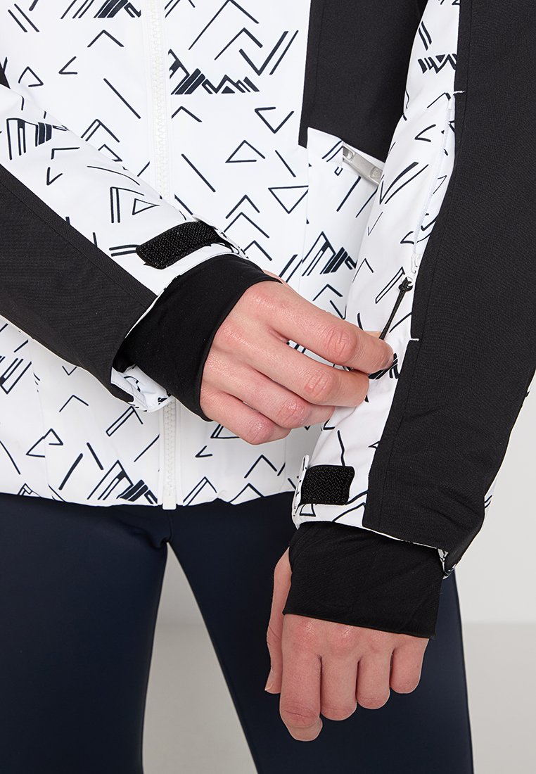 Biała i czarna kurtka z geometrycznymi wzorami, zamkiem błyskawicznym oraz czarnymi mankietami z otworami na kciuki. Tkanina wydaje się strukturalna, odpowiednia do odzieży sportowej.