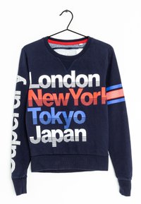 Sudadera navy con cuello redondo, que presenta un texto audaz en blanco, rojo y azul: "Londres", "Nueva York", "Tokio" y "Japón". Rayas horizontales en la manga.
