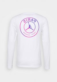 Vit långärmad skjorta med en cirkulär grafik som har "PARIS" och "SAINT-GERMAIN" i gradientlila och rosa, samt en silhuett av en hoppande figur.