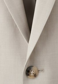Revers et col de blazer beige avec un seul bouton en écaille de tortue fixé sur le devant du vêtement.