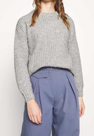 Maglione grigio a maglia con un motivo testurizzato, polsini a coste e una vestibilità morbida, abbinato a pantaloni sartoriali alti di colore blu chiaro.
