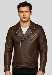 Uomo che indossa una giacca da motociclista in pelle marrone scuro con tasche con zip, bottoni argentati e una cintura, sopra una maglietta bianca su uno sfondo grigio.