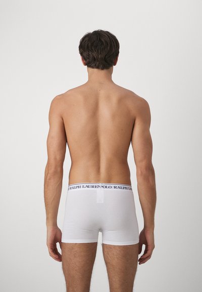 Weiße Baumwoll-Boxershorts mit einem schwarzen Logo-Bund, die eine enge Passform und eine mittellange Beinlänge haben, von hinten gezeigt.