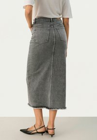 Falda midi de mezclilla gris con cintura ajustada, dobladillo deshilachado y dos bolsillos traseros. Combinada con zapatos de tiras negros.