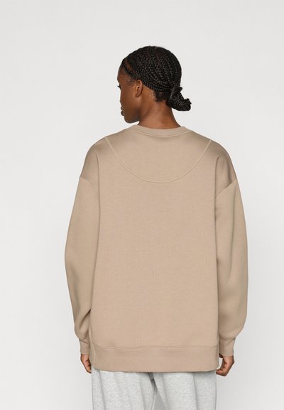 Μπεζ φούτερ με στρογγυλή λαιμόκοψη, χαλαρή γραμμή στους ώμους και ριμπ μανσέτες. Λείο ύφασμα με ελάχιστες ραφές στο πίσω μέρος.