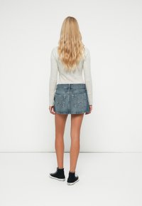 Denim mini seelik, millel on veidi kulunud serv ja kaks taga taskut, millel on tähekujulised õmblused. Seljas on heledhalli pikakäistega särk.